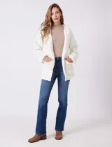 Campera tipo teddy de textura suave y esponjosa en color blanco, con cierre frontal mediante botones y detalles de apliques en cuero sintético negro en la solapa. Presenta bolsillos frontales y un diseño cómodo y abrigado.