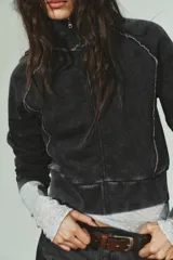 Sudadera corta negra con efecto lavado, cuello alto y manga larga. Presenta costuras marcadas a contraste en color blanco y cierre frontal con cremallera metálica.