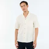 Camisa de manga corta color blanco con sutiles rayas verticales oscuras, cuello camisero tipo cubano y cierre frontal con botones.