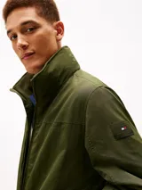 Campera Tommy Hilfiger de color verde militar, con cuello alto, cierre frontal de cremallera y bolsillos laterales. Confeccionada en poliamida, presenta un diseño clásico y versátil con el logo de la marca bordado discretamente en el pecho.