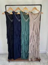 Vestido largo negro de seda italiana con diseño sin mangas de bretel ancho y escote en V profundo con detalles de paillettes plateados. Presenta múltiples capas con volados y bordes deshilachados que aportan movimiento y una caída fluida.