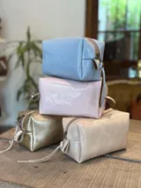 Neceser de cuero con acabado brillante, cierre superior y tirador de cuero con detalle de cinta estampada.