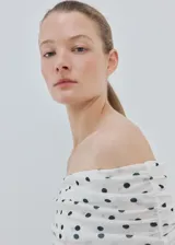 Camiseta blanca de malla con estampado de lunares negros, escote palabra de honor cruzado con fruncidos y manga larga.