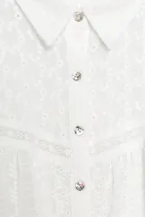 Blusa corta de color blanco con diseño de bordados perforados, cuello solapa, cierre frontal con botones y mangas largas abullonadas.