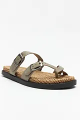 Sandalia plana negra con base de fibra trenzada y tiras cruzadas ajustables con hebillas metálicas.