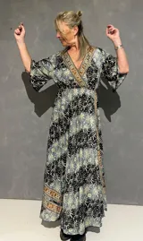 Vestido largo cruzado al frente de seda estampado en tonos azules, negros y dorados, con escote en V ribeteado, mangas 3/4 fluidas y elástico en la parte trasera de la cintura.