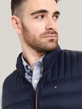 Chaleco acolchado de nailon en color azul marino, con cuello alto, cierre frontal de cremallera con detalles distintivos de la marca y bolsillos laterales con cierre. Presenta el logo de Tommy Hilfiger bordado en el pecho.