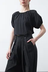 Pantalón baggy negro de silueta relajada con volumen amplio y caída fluida. Presenta detalles de ajuste con hebillas metálicas en el bajo y un cinturón de tela con hebilla metálica en la cintura.