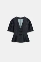 Blusa de denim oscuro con escote en pico, mangas cortas abullonadas y diseño peplum con bajo evasé. Presenta cierre frontal con alamares decorativos y cierre lateral con cremallera oculta.
