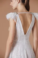 Vestido corto de encaje blanco con silueta evasé, escote en V y detalle de plumas desmontables en los hombros. Presenta una textura con destellos sutiles y cintura definida.