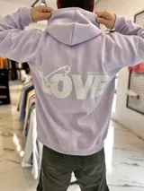 Canguro oversize lila con capucha y gran estampado blanco en la espalda con la palabra "LOVE" y un imperdible.