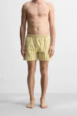 Short de baño confeccionado en tejido técnico, con diseño de rayas verticales amarillas y verdes sobre fondo blanco. Cuenta con cintura elástica ajustable con cordón, bolsillos laterales y bolsillo trasero con vivo.