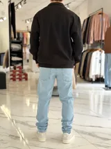 Buzo de felpa color beige con medio cierre frontal y cuello alto. Presenta estampado frontal con texto en contraste y diseño de estilo urbano.
