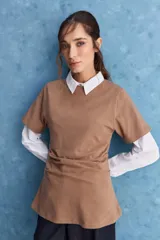 Remera marrón de manga corta con cuello redondo y pliegues laterales que generan un efecto drapeado.
