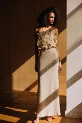 Vestido largo color tostado con aplique de flor voluminosa en el escote strapless y acabado con sutiles lentejuelas.