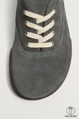 Zapatilla deportiva barefoot fabricada en piel con acabado serraje de color marrón, con cordones en contraste y suela fina de goma.