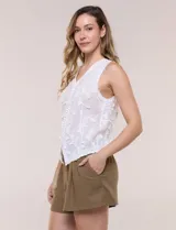 Blusa sin mangas blanca de puro algodón liviano, con escote en V, bordados florales en relieve, cartera frontal abotonada y terminaciones con festón calado.