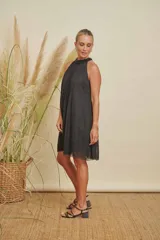 Vestido corto negro con escote halter adornado con perlas, diseño holgado y detalles de perlas en la parte inferior de la falda.