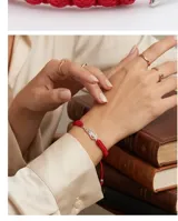 Pulsera de hilo rojo tejida en macramé con dije central en forma de ala de plata 925 y terminaciones con esferas de plata. Diseño regulable.