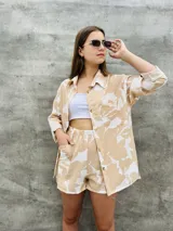 Camisa de corte oversize con estampado botánico en tonos beige y blanco, cuello clásico, cierre frontal con botones y bolsillo en el pecho.