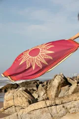 Pareo rectangular fucsia con estampado de sol dorado y borde con diseño geométrico en tonos naranja y marrón.