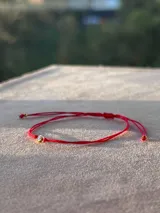 Pulsera de hilo rojo regulable con cierre de nudo corredizo y un punto de luz central engarzado en oro laminado.