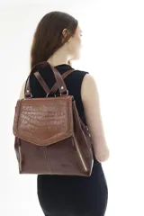Mochila de cuero vacuno marrón con acabado pulido, solapa en forma de V y costuras decorativas. Cuenta con cremalleras laterales y asas ajustables.