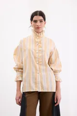 Camisa holgada de algodón con estampado de rayas en tonos amarillos, naranjas y grises. Presenta cuello alto con volados, cierre frontal con botones dorados y mangas largas abullonadas con puños con volados.