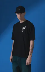 Remera de manga corta y cuello redondo con calce oversize. Presenta una estampa frontal en color crema con diseño artístico de un ángel y una rosa, acompañada de frases en español. Confeccionada en algodón premium.