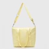 Bolso tipo tote color amarillo, de diseño acolchado con costuras horizontales. Cuenta con doble asa de mano y una correa larga ajustable y extraíble. Incluye un pequeño detalle de etiqueta lateral.