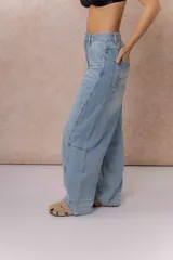 Jean de tiro alto con silueta balloon oversize, confeccionado en denim rígido de lavado celeste desgastado. Presenta costuras curvas que aportan volumen, cierre y botón frontal, y bolsillos funcionales.