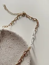 Collar de cadena con eslabones combinados en metal dorado y acrílico blanco.