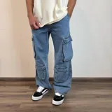 Pantalón de jean estilo cargo con corte baggy, color azul lavado. Presenta cuatro bolsillos laterales de gran tamaño con solapa y cierre de botones, diseño de pierna ancha y tiro medio.