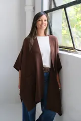 Poncho abierto de color marrón chocolate, con diseño de corte asimétrico, mangas amplias y bolsillos frontales aplicados.
