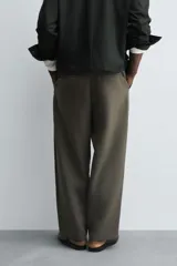 Pantalón de corte relajado en color verde militar, con diseño de pliegues frontales, bolsillos laterales y cierre de cremallera con botón.