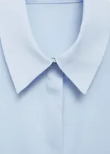 Camisa de corte recto y tejido fluido, color celeste, con cuello camisero, cierre frontal de botones y mangas largas con puños abotonados.