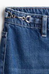 Jeans de tiro alto, pierna ancha y corte recto, confeccionado en denim de algodón rígido de color azul medio. Presenta un detalle de herrajes metálicos en la cintura.