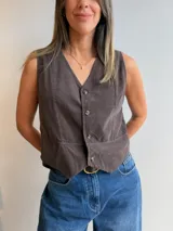 Chaleco de pana fina color marrón oscuro, con escote en V, cierre frontal de botones y corte entallado.