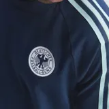Remera de estilo urbano Adidas inspirada en la selección de fútbol de Alemania. Es de color azul marino con las icónicas tres tiras en celeste sobre los hombros y mangas. Presenta el logo del trébol de Adidas en blanco en el pecho derecho y el escudo de la federación alemana en el izquierdo.