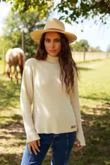 Polera de tejido de punto acanalado en color beige, con cuello alto y mangas largas. Presenta un pequeño bordado en el ruedo inferior.