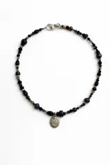 Collar corto de cuentas facetadas en tonos oscuros con un dije colgante ovalado de metal plateado con relieve.