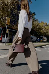 Bolso pequeño tipo satchel, color borgoña oscuro, con doble asa de mano y correa bandolera extraíble. Presenta dos compartimentos exteriores con cierre de cremallera metálica y un compartimento interior con cierre imantado.