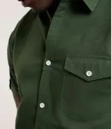 Camisa de hombre de manga corta color marrón, confeccionada en lino y algodón. Presenta cuello clásico, botonadura frontal, bolsillo en el pecho y mangas con botón para enrollar.