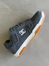 Championes DC modelo Sarah, color gris oscuro con detalles en blanco y suela de goma color caramelo. Presentan el logo de DC en blanco en el lateral y están inspirados en la cultura skate.