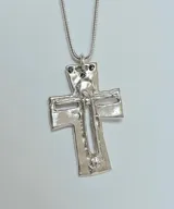 Collar con dije de cruz de diseño artesanal con acabado irregular y calado central, suspendido de una cadena tipo serpiente. El dije presenta tres pequeñas incrustaciones de piedras oscuras en la parte superior.