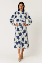 Vestido midi de corte camisero con estampado floral abstracto en tonos azul y blanco. Presenta cuello clásico, cierre frontal con botones, mangas largas con frunces en los hombros y diseño holgado.