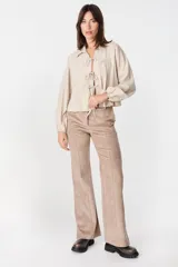 Blusa de algodón color beige con cuello camisero, mangas largas abullonadas con puños elásticos y cierre frontal mediante tres lazos para anudar.