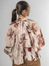 Camisa de seda italiana con estampado floral en tonos rosados, marrones y verdes. Presenta cuello alto con volados que caen en cascada sobre el frente y mangas largas abullonadas con puños ajustados.
