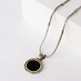Collar con cadena de eslabones trenzados en plata con detalles en oro, que sostiene un dije circular con piedra ónix negra central y borde en oro.