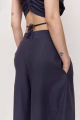 Pantalón azul marino de tiro alto con cintura ancha y pliegues frontales que aportan volumen y una caída suelta y fluida, con diseño envolvente en la cadera y bolsillos laterales.